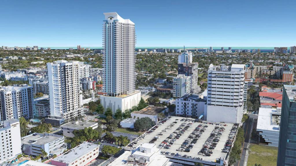 An aerial architectural rendering of the South Tower in Fort Lauderdale, FL. The sleek, white 43-story residential tower stands prominently in the center, featuring blue vertical accents and a unique curved roofline. It is surrounded by the dense urban landscape of downtown Fort Lauderdale, with other high-rise buildings, parking structures, and the Atlantic Ocean visible on the horizon under a clear blue sky.