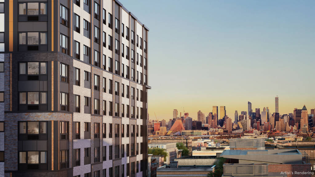 A view from an upper floor of The Station residential building in New Jersey, looking past the modern gray and tan brick facade toward the expansive New York City skyline at sunset.